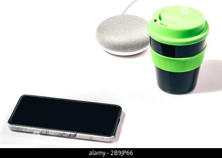 Digital Assistant concept. Smart speaker with smartphone and reusable coffee cup with green lid on white background. Stock Photo