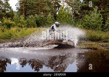 motocross rider riding a puddle in forest trail. splashes and drops of water Stock Photo