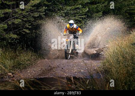 enduro racer riding on water with splashes motocross race in forest Stock Photo