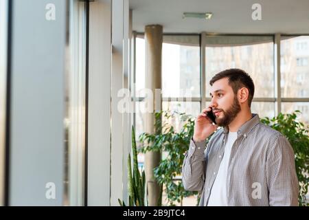 Phone conversation in urban modern office. Smart beard man is negotiating by smartphone. Attractive businessman freelancer in cafe. Young caucasian Stock Photo