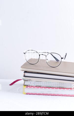 Collection of different colorful note books for notes and annotations with glasses on the top on a white table against light grey wall, copy space. Wo Stock Photo