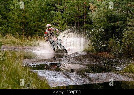 motocross rider riding in puddle with splashes, forest enduro race Stock Photo