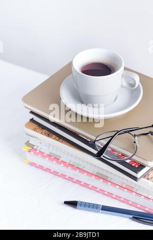 Set for study of work from different colorful books and notepads with glasses and cup of coffee on the top on a white table against light grey wall, c Stock Photo