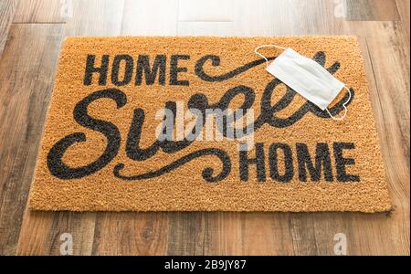 One Medical Face Mask Rests on Home Sweet Home Welcome Mat Amidst The Coronavirus Pandemic. Stock Photo