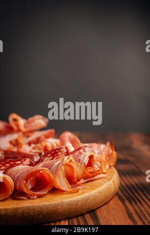Assorted meat snacks on a wooden cutting board. Sausage, ham, bacon, smoked meats. Stock photo of meat products with blank space. Stock Photo