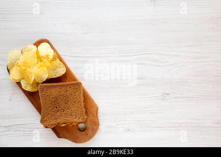 Homemade Peanut Butter Pickle Sandwich with Potato Chips on a rustic wooden board on a white wooden surface, overhead view. Flat lay, top view, from a Stock Photo