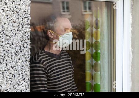 Man wearing a mask looking out of window Stock Photo
