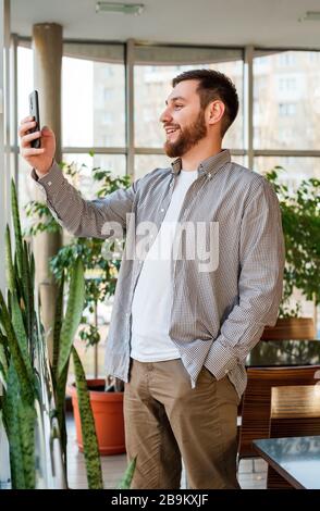 Phone conversation by video calling in urban modern office or cafe. Smart man negotiating by smartphone. Happy smiling bearded businessman freelancer Stock Photo