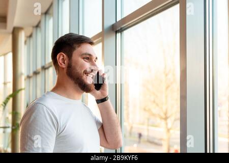 Phone conversation in urban modern office. Smart man negotiating by smartphone.Happy smiling bearded businessman freelancer in cafe.Young caucasian Stock Photo