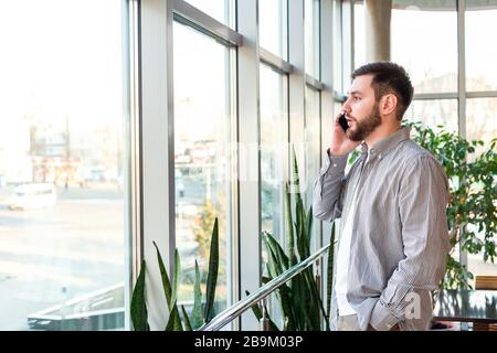 Phone conversation in urban modern office. Smart beard man is negotiating by smartphone. Attractive businessman freelancer in cafe. Young caucasian Stock Photo
