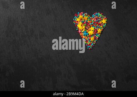Sprinkle heart shape background. Sprinkle in the form of stripes, balls, stars on a black background. copy space. concept of an Easter plan. top view photo Stock Photo