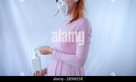 An expectant mother with sanitizer cleaning hands during pandemic, feeling bad and sick at home and taking care of her unborn baby. Stock Photo