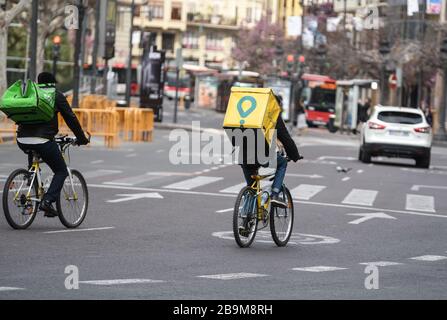 Two distributors of the Glovo and Uber companies move around the empty city through the quarantine by bicycle Stock Photo