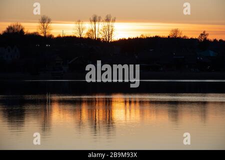 Beautiful sunset reflected on the water on a blue lake or river with silhouette of forest Stock Photo