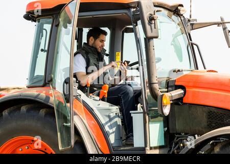 Male Agricultural Worker On tractor Using Digital Tablet. Stock Photo