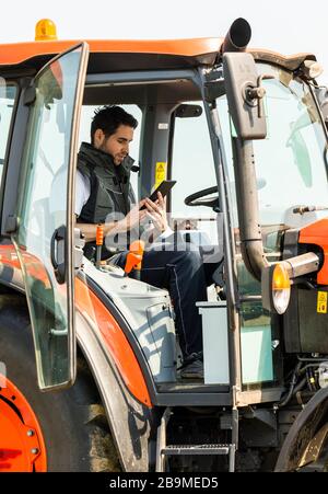 Male Agricultural Worker On tractor Using Digital Tablet. Stock Photo