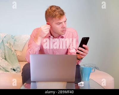 Blonde caucasian businessman is working from home on his computer on a sofa with a light blue background. Stock Photo
