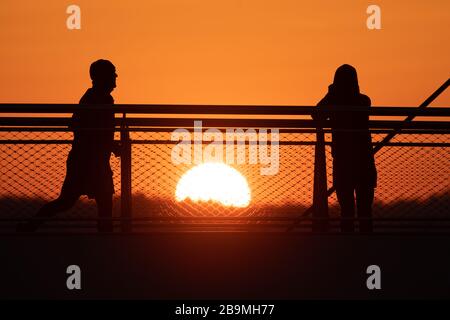 24 March 2020, Saxony, Dresden: Passers-by watch the sunset from the pier bridge. Photo: Sebastian Kahnert/dpa-Zentralbild/dpa Stock Photo