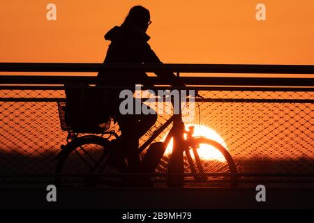 24 March 2020, Saxony, Dresden: A female cyclist crosses the pier bridge at sunset. Photo: Sebastian Kahnert/dpa-Zentralbild/dpa Stock Photo