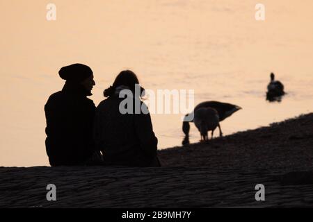 24 March 2020, Saxony, Dresden: Passers-by sit on the banks of the Elbe at sunset. Photo: Sebastian Kahnert/dpa-Zentralbild/dpa Stock Photo