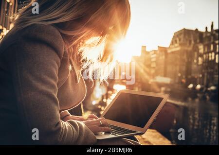 Woman using credit card online with her laptop during beautiful sunset in the city Stock Photo