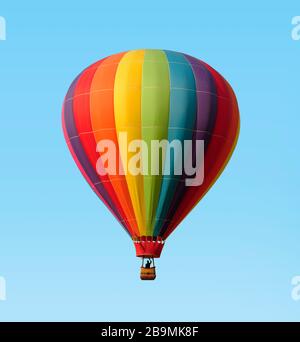Rainbow colored hot-air balloon floating against a blue sky. Pilot in silhouette. Stock Photo