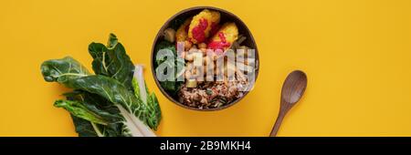 Wide view image of delicious and nutritious vegan meal served in buddha bowl. Over yellow background with fresh swiss chard on the side. Wide view ima Stock Photo