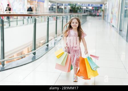 Cheerful preschool girl walking with shopping bags. Pretty smiling little girl with shopping bags posing in the shop. The concept of shopping in stores. Stock Photo