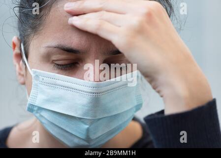 Close-up woman wearing a face surgical mask holding her head and having headache on gray background. Selective focus. Flu, illness, pandemic concept Stock Photo