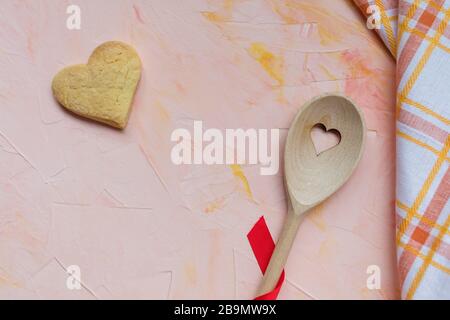 Stirring spoon, heart shaped butter cookie and a kitchen towel on a pink background . Spring holidays cooking and celebration concept. Top view, flat Stock Photo