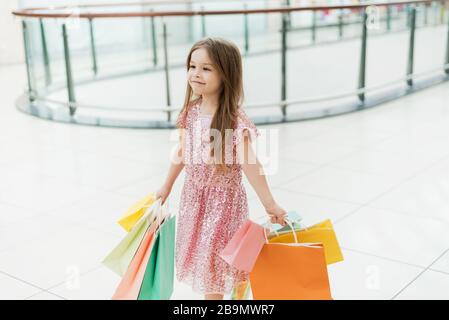 Cheerful preschool girl walking with shopping bags. Pretty smiling little girl with shopping bags posing in the shop. The concept of shopping in stores. Stock Photo