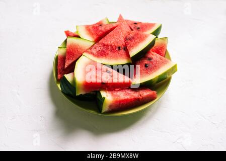 Fresh watermelon in a green plate on a white table. Slices of a watermelon in a triangular shape. Natural background with shadows Stock Photo