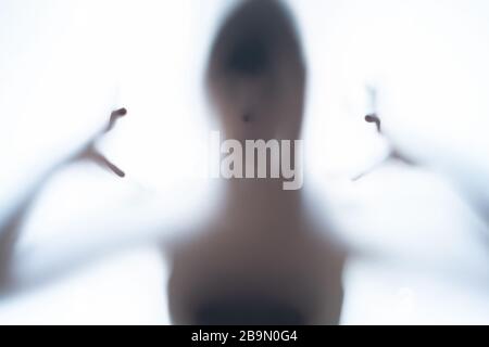 Blurred silhouette shadow of a terrorific body shape behind a white background showing head and creepy fingers. Horror concept of a visitor from out o Stock Photo