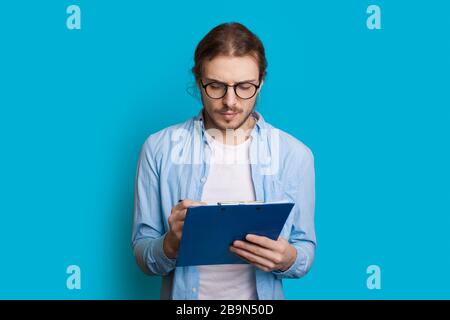 Young caucasian entrepreneur with long hair and beard writing something on a blue wall Stock Photo