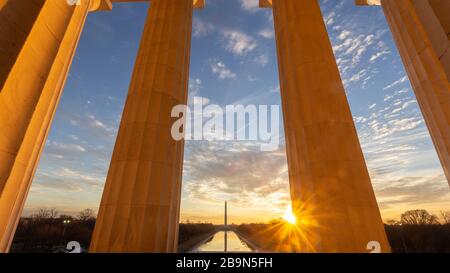 The sun rises over Washington, D.C. and the Lincoln Memorial Reflecting Pool as seen from inside the Lincoln Memorial and it's stone pillars Stock Photo