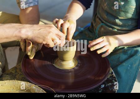 Hands over a Potters wheel sculpt from yellow clay dishes. Master and disciple Stock Photo
