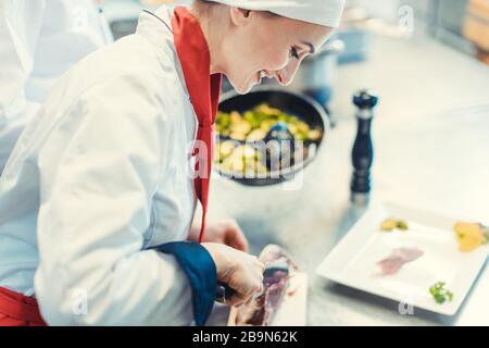 Chef cook in fancy restaurant kitchen slicing ham for a dish Stock Photo