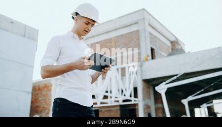 Caucasian builder looking in a tablet while making the future building plan while wearing a helmet Stock Photo