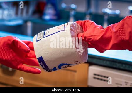 Two people wearing bright red latex gloves hand off a roll of toilet paper. In the background are elements of a brightly lit kitchen. The images illus Stock Photo
