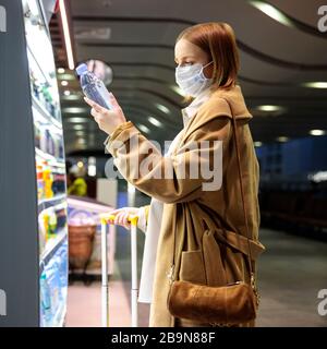 Caucasian woman customer wearing facial protective mask in airport, buying and choosing water bottle, reads information on a label. Purchase of food d Stock Photo