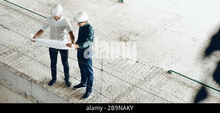 Upper view portrait of two engineers looking at the building's plan while holding a map Stock Photo