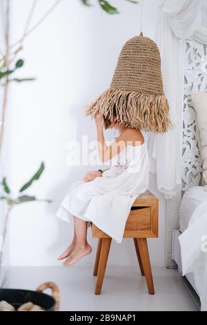 Playful little girl in a white dress wearing lampshade as a hat Stock Photo