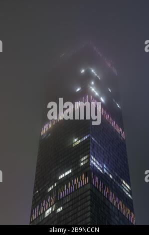 Abstract hi-tech background of fragment modern elevation office buildings of steel and glass with lights switched at night in the fog Stock Photo