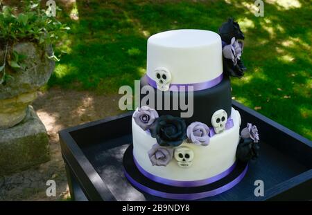 Beautiful bridal cake in white, black and purple decorated with flowers and skulls Stock Photo