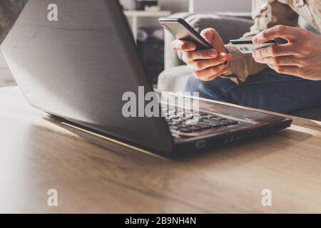 Mеn entering secure code on smartphone while shopping online using laptop with bank card Stock Photo