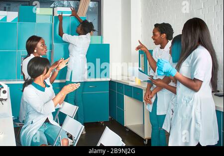 Female African medical students, young graduates or doctors discuss ongoing project. Energetic expressive group discussion in research facility. Testi Stock Photo