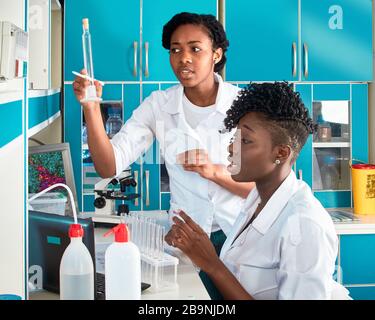 Two female African medical students or young graduates in research or medical test laboratory performing various testing on samples. Microscopic analy Stock Photo