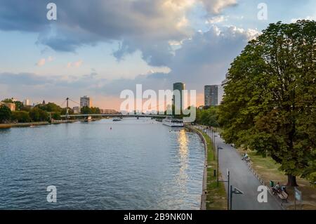 Frankfurt am Main with Holbeinsteg footbridge, touristic boat and promenade along Main river at sunset with overcast dramatic sky. Frankfurt is the fi Stock Photo