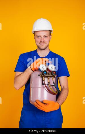A male air conditioning repairman is holding a freon cylinder in his hands to air-condition the air conditioner. Refueling freon air conditioners. Stock Photo