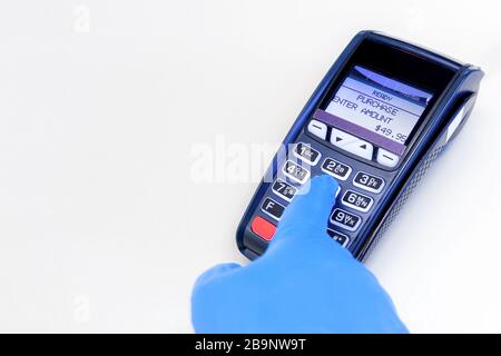 A hand wearing a blue latex protective glove using a credit card terminal. Machine is type used in retail to process credit card payments. Stock Photo